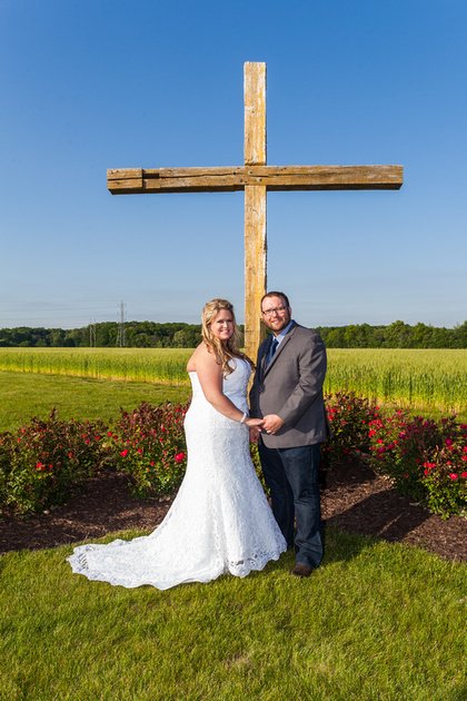 The bride and groom standing outside by a wooden cross